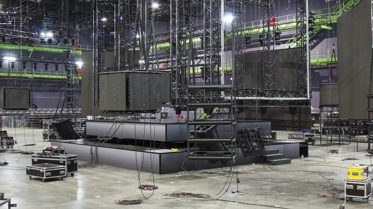 Installation of professional stage, sound, light and video equipment for a tv show. Led screens. Stage lighting equipment is clamped on a trusses. Line array speakers. Flight cases.