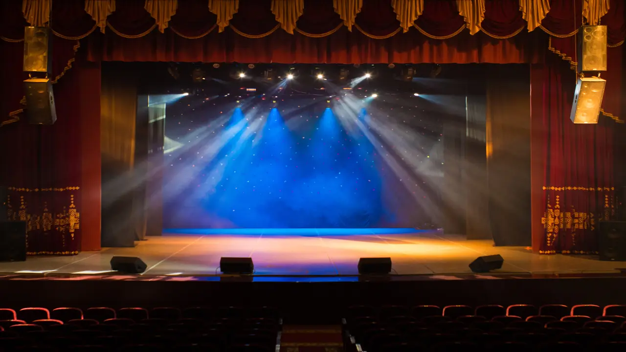 An empty stage of the theater, lit by spotlights and smoke