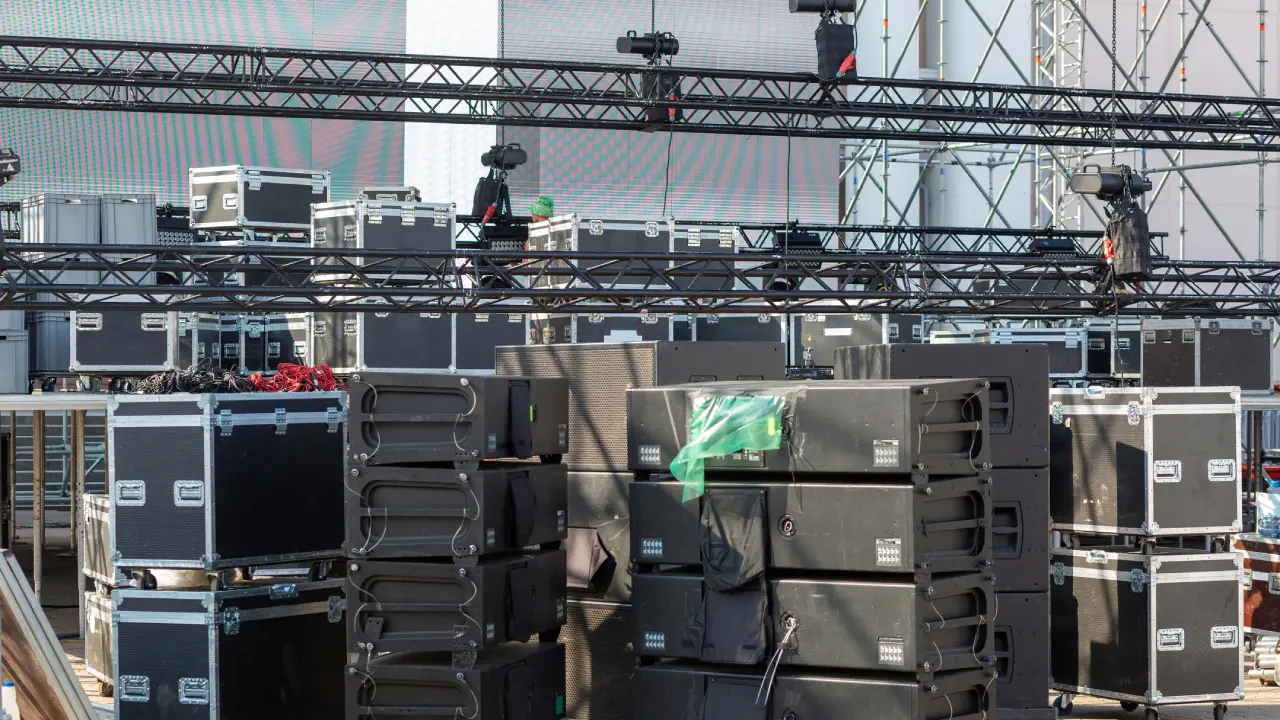 A large area is filled with stacked equipment cases and staging gear, being prepared for an upcoming event. Crane structures are poised above, ready for installation.